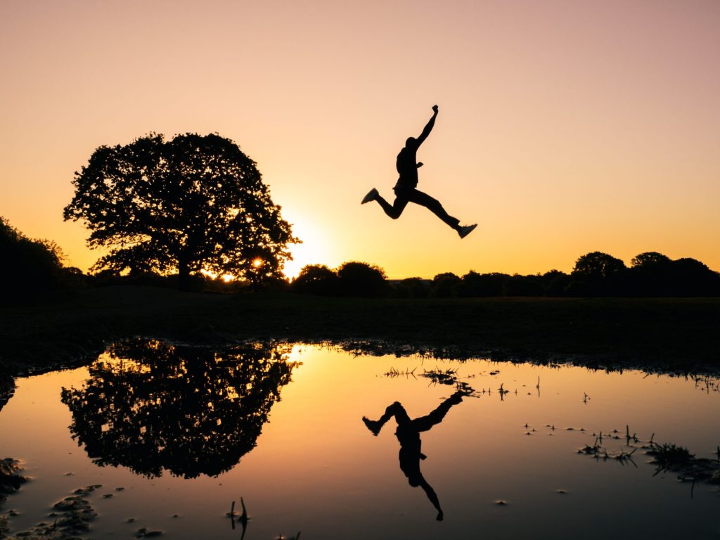 Person jumping over water with sunset
